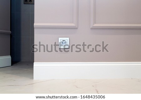 electrical outlet on the brown wall above the baseboard and marble floor Royalty-Free Stock Photo #1648435006