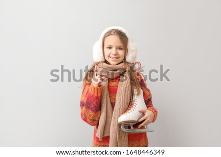 Cute little girl with ice skates and raised index finger on light background