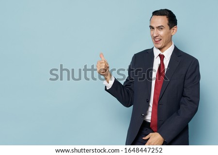 A man on a blue background in a classic suit is gesturing with his hands