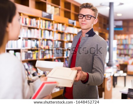 Handsome guy helping young female student in search of books in bookshop