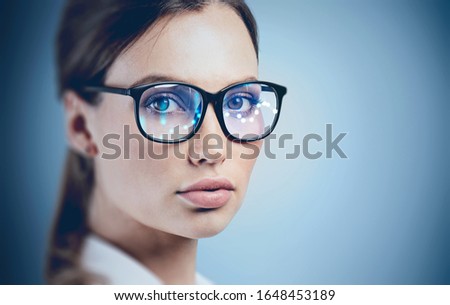 Face of beautiful young woman in glasses with graph reflected in them. Concept of augmented reality and hi tech. Blurry image, mock up Royalty-Free Stock Photo #1648453189