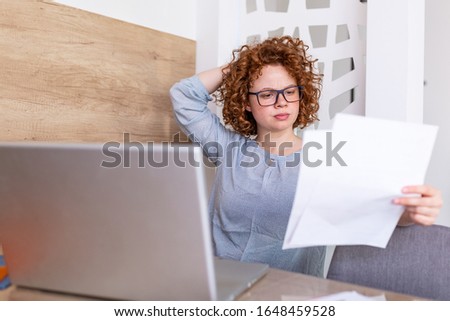 Upset business woman looking at documents and paperwork she is sitting at the table at workstation. young woman in her office working on laptop