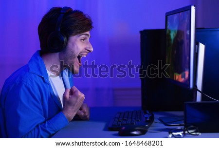 Winner. Excited Gamer Man Winning Computer Game Celebrating Victory Screaming And Shaking Fists Sitting At PC Indoor. Free Space