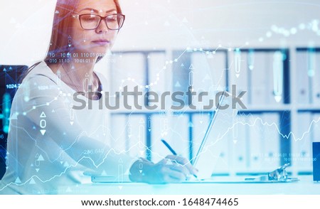 Young European businesswoman in glasses writing financial report in blurry office with double exposure of digital graph. Concept of trading and market analysis. Toned image