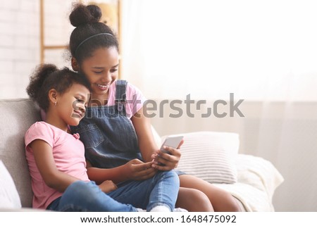 New generation fun. African teenage girl teaching showing cellphone to her sister, free space