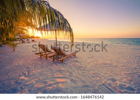 Beautiful tropical sunset scenery, two sun beds, loungers, umbrella under palm tree. White sand, sea view with horizon, colorful twilight sky, calmness and relaxation. Inspirational beach resort hotel