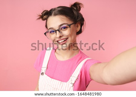 Photo of happy beautiful girl in eyeglasses taking selfie photo and smiling isolated over pink background