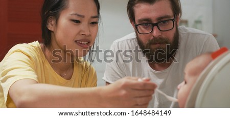 Medium close-up of a young couple feeding their baby
