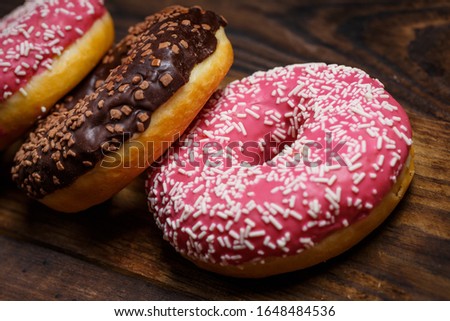 Chocolate and pink fresh donuts on a wooden breakfast table