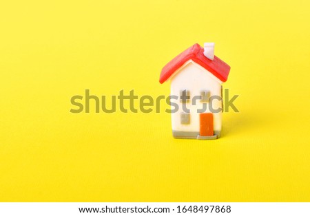 Miniature toy house with red roof on a yellow background. 