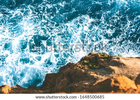 top view of sea waves hitting rocks on the beach with turquoise blue sea water. rock cliff seascape in Atlantic ocean coastline. splashing water in coast with rocks with spray and foam.