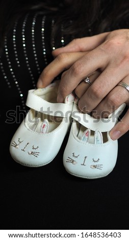 Couple hands holding baby shoes, couple expecting baby, family photo of happy future parents, white shoes on black background 