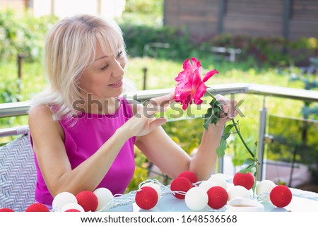 Woman lady blond looks at a natural flower close-up face. A woman is enjoying the smell of a rose. The concept of Women's Day, Valentine's Day, spring and summer, perfume and cosmetics.