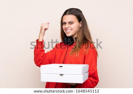 Pizza delivery girl holding a pizza over isolated wall celebrating a victory