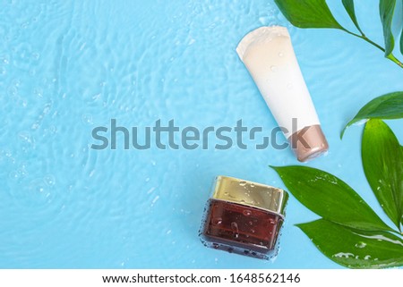 Sunscreen cream spf lotion to remedy skin from sun with green leaves on blue water surface of pool, top view. Concept ultraviolet protection, summer cosmetics. Natural organic beauty product