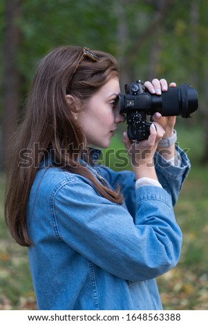 Portrait of a freelance photographer outdoors. Beautiful Caucasian woman takes a picture on a black camera