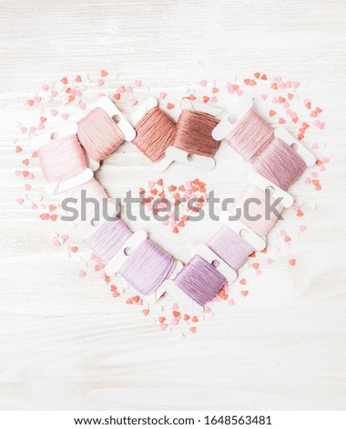 Threads for handwork is laying in shape of a heart with small candies around. 