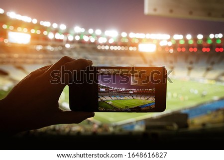 Smartphone photographing football game on the stadium.