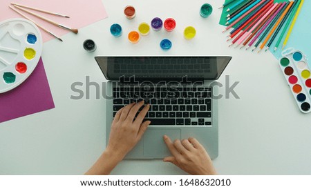 Top view of female hands using laptop and various colorful drawing tools