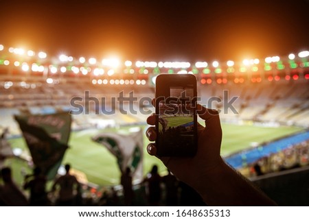 Smartphone photographing football game on the stadium.