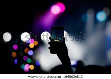 Silhouette of hand using smartphone to take pictures and videos at live music show