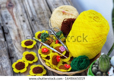 The picture is enlarged. Sunflower knitting equipment is placed on an old wooden table, crochet, scissors and yarn, green, yellow, green.