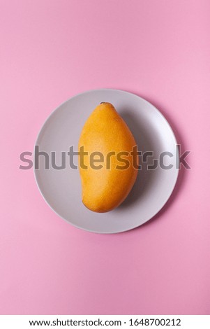 Fresh yellow mango on a plate and pink background. Ripe exotic fruit on a dish. Pastel background. 