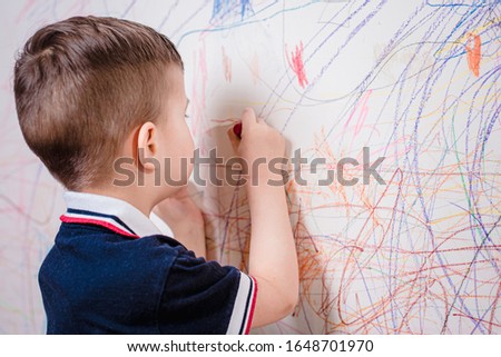 The child draws on the wall with colored chalk. The boy is engaged in creativity at home