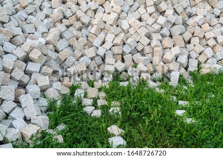 Stone paving stones, for laying the road, poured into a pile for construction work. Close-up. On the green grass.