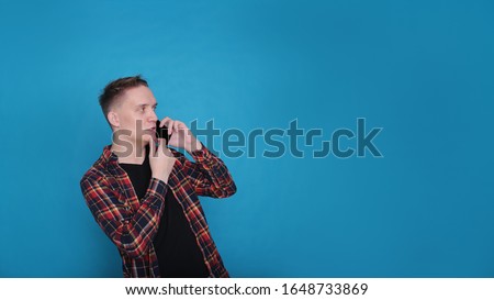 portrait emotional classy stylish young guy in a black t-shirt and a checked shirt on a bright blue background
