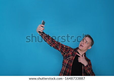 portrait emotional classy stylish young guy in a black t-shirt and a checked shirt on a bright blue background