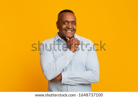 Positive mature african man touching his chin, orange background