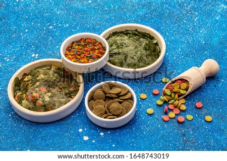 Assorted different types of food for aquarium fish. Flakes, spirulina, pills, mixture. Navy blue sea background, close up
