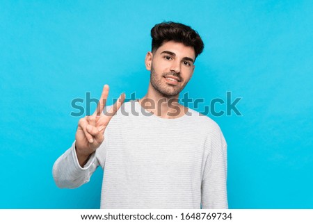 Young man over isolated blue background smiling and showing victory sign