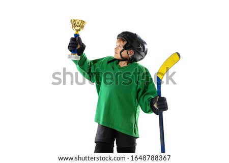 Champion. Little hockey player with the stick on ice court and white studio background. Sportsboy wearing equipment and helmet training. Concept of sport, healthy lifestyle, motion, movement, action.