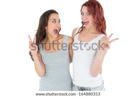 Portrait of two cheerful female friends gesturing peace sign over white background