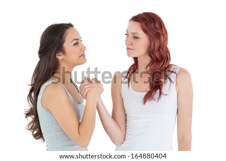 Two casual young female friends arm wrestling against white background