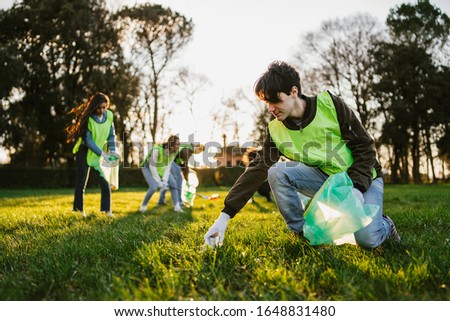 Group of friends during a volunteer garbage collection event in a park at sunset - Millennial having fun together - Happy people cleaning area with bags - Ecology concept Royalty-Free Stock Photo #1648831480