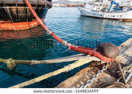 Ships moored in the port. Large rusty mooring bollard with hawsers, chain and ropes on the quay of the harbor. La Spezia, Liguria, Italy, Europe