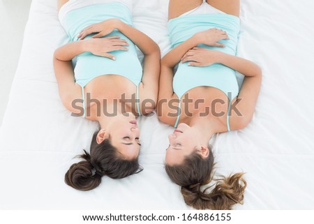 High angle view of two young female friends in teal tank tops sleeping in bed at home
