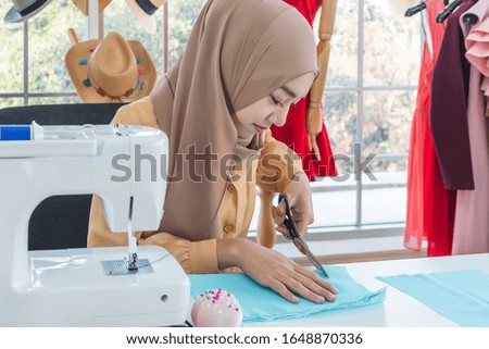 Young beautiful Muslim fashion designer using scissors in Tailor shop.