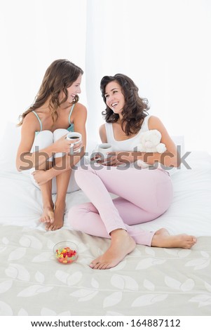 Cheerful young female friends with coffee cups in bed at home