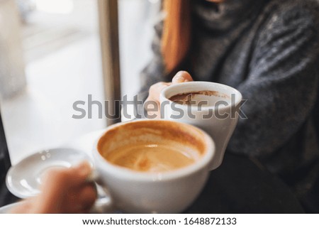 Closeup image of a woman and a man clinking coffee mugs in cafe