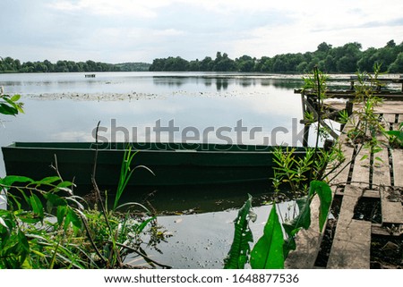 Abandoned Old Wooden Fishing Boat Near Pier In Summer Lake Or River. Beautiful Summer Sunny Day with amazing nature view. Forsaken Boat. Europe Nature.