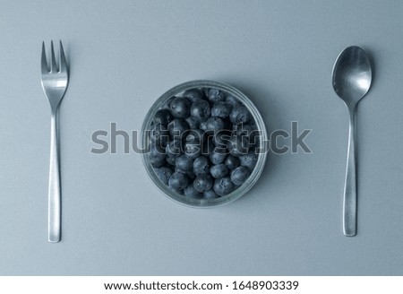 Delicious transparent glass bowl of fresh organic blueberries and a fork and spoon on a modern kitchen countertop