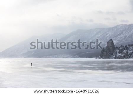 Woman walking on the frozen ice of lake Baikal on a windy day with a snow storm. Lake Baikal, Siberia, Russia.