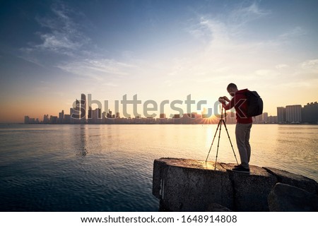 Photographer with camera on tripod photographing urban skyline at sunrise. Abu Dhabi, United Arab Emirates.