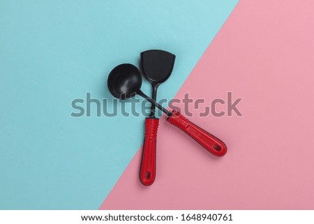 Toy kitchen tools on a pink-blue pastel background. Kitchen spatula, ladle. Top view