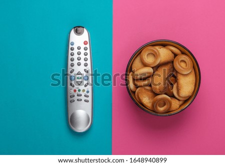 TV remote control and a bowl of crackers on a pink blue background. Watching the TV. The concept of home rest after work. Top view.