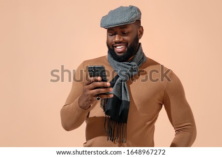 Handsome man uses the phone, checks for new message. Photo of african man in stylish casual clothes on beige background.